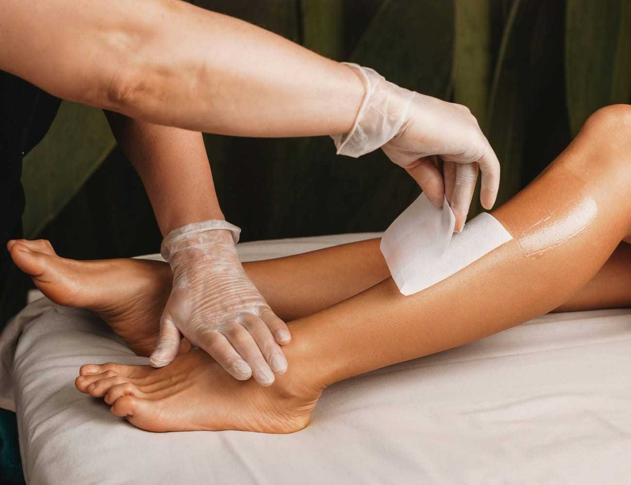 Waxing treatment on a person's legs, therapist wearing gloves.