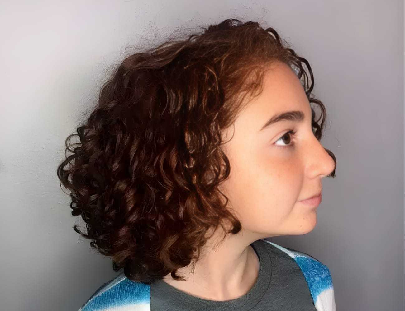 Young person with curly hair looking to the side, wearing a blue and gray patterned top.