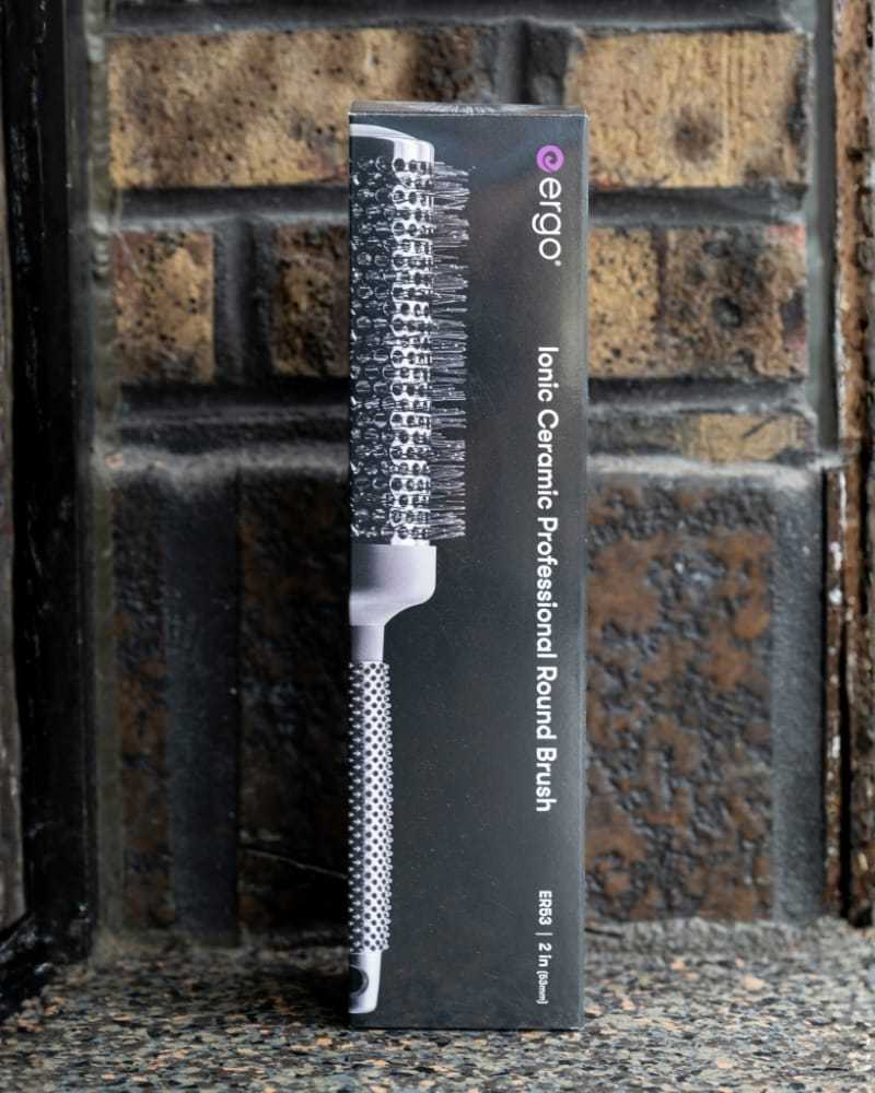 Professional round hairbrush in sleek packaging against a brick wall.