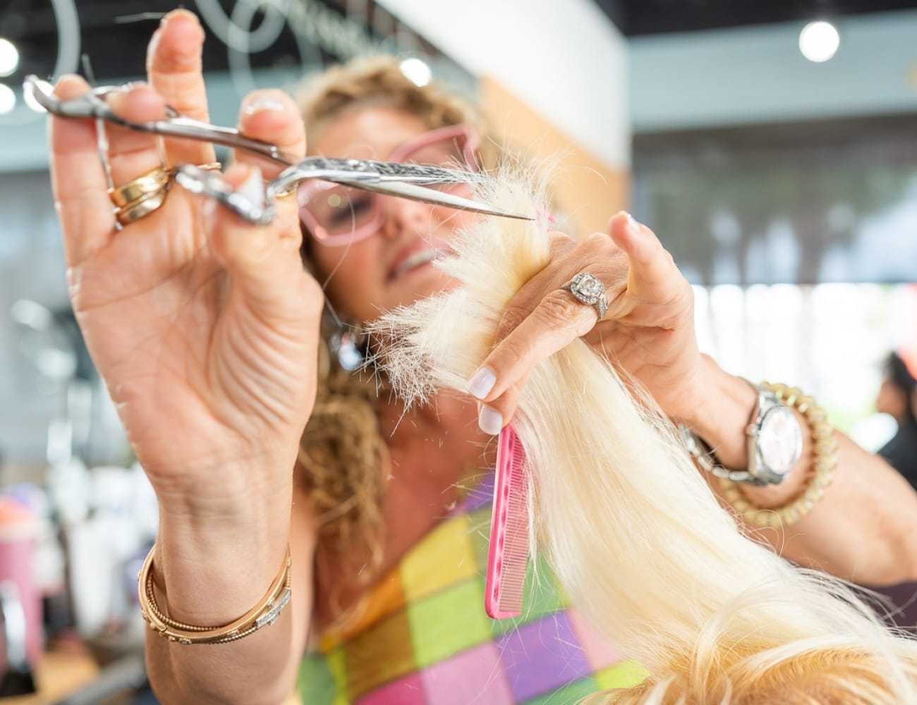 Hairdresser cutting blonde hair with scissors and comb in salon.