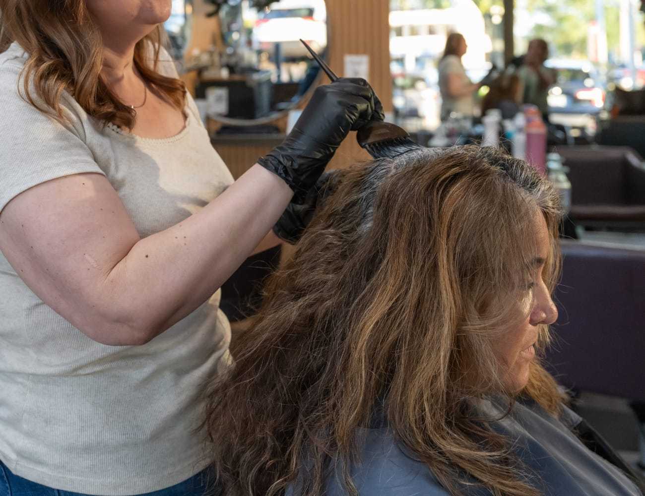 Hairdresser applying dye to woman's hair at a salon.