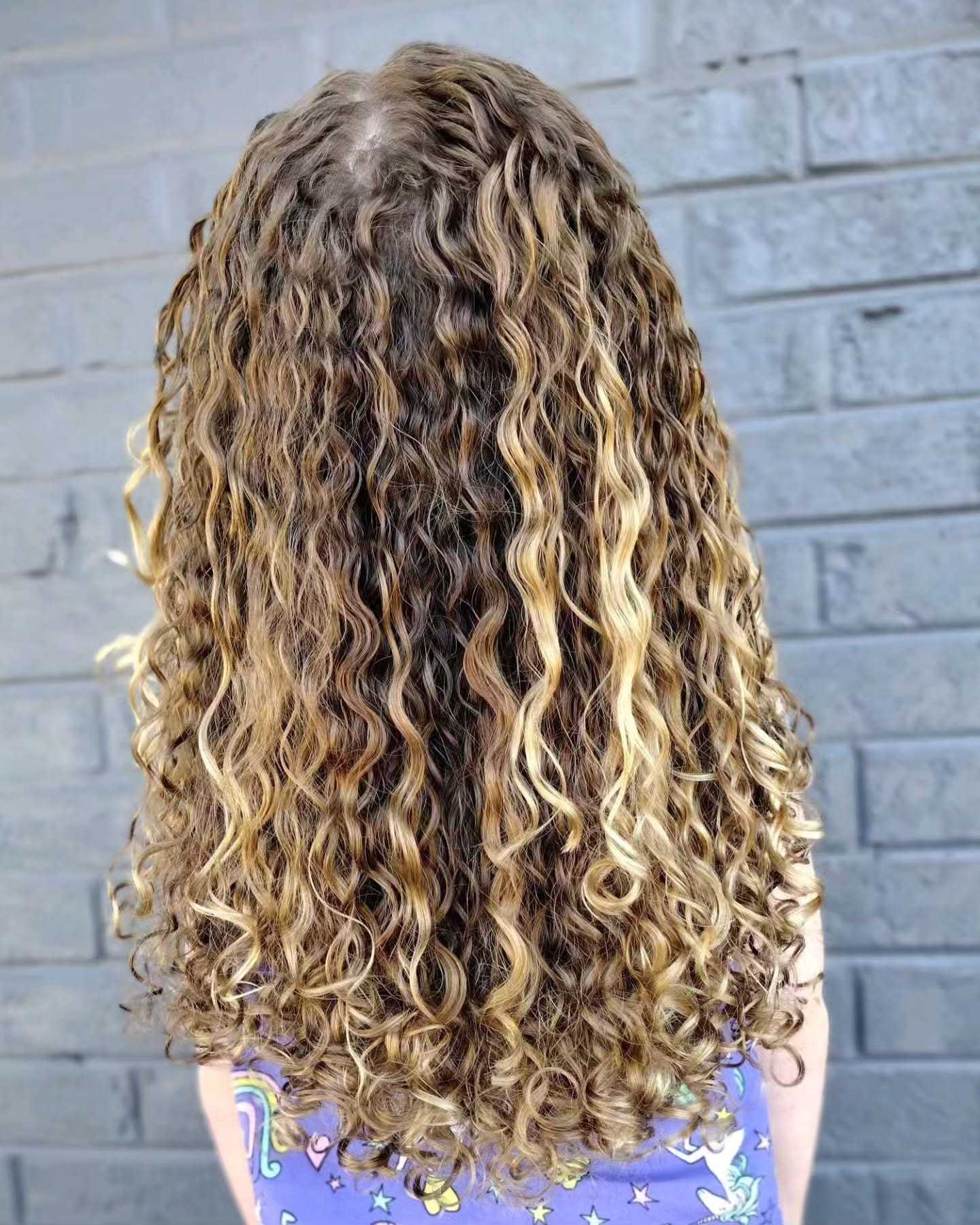 Curly hair with blonde highlights in front of a gray brick wall.